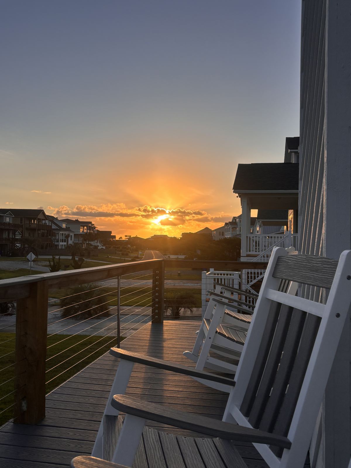 White rocking chairs on the deck facing a bright orange sunset